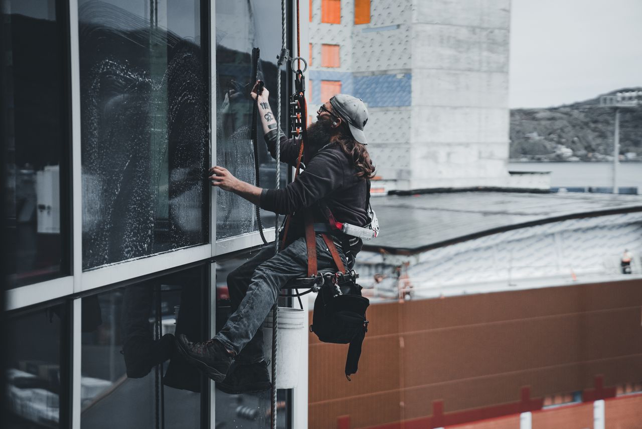 creative A man cleaning skyscraper windows with a harness, showcasing urban high-rise work.